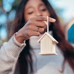 Close-up of a woman holding a wooden house symbolizing real estate or homeownership.
